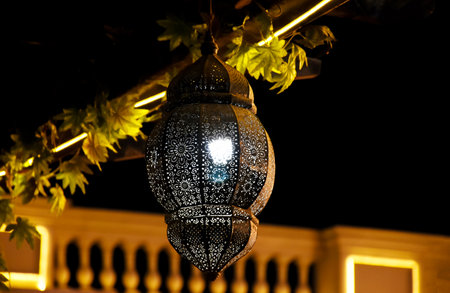 A close-up of an intricately designed metal lantern glowing warmly in the nightの写真素材