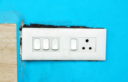 A white electrical switchboard with multiple switches and a socket installed on a bright blue wall.