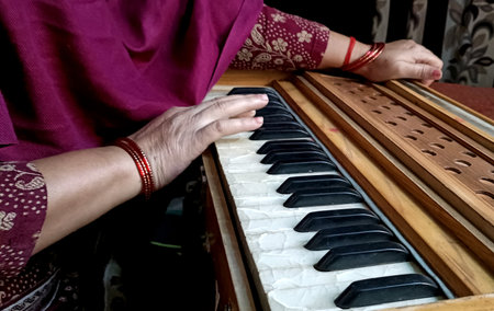 A close-up view of a personâ€™s hand playing a harmonium, highlighting the keys and wooden...