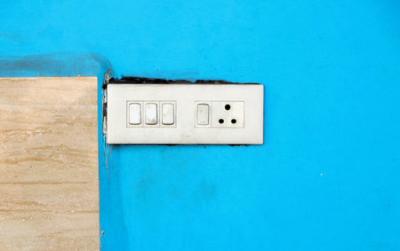 A white electrical switchboard with multiple switches and a socket installed on a bright blue wall.