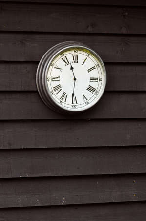 Clock with Roman numerals on brown wooden wall 