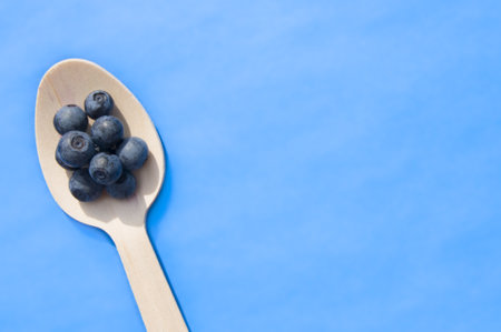 Flat lay of recycled spoon and juicy fresh blueberries on color table. Space for text. Isolated ripe sweet bilberry fruits in eco spoon on sky blue background. Copy Space. Healthy raw vegetarian foodの写真素材