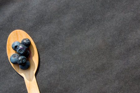 Flat lay of recycled spoon and juicy fresh blueberries on rough table. Space for text. Isolated ripe sweet bilberry fruits in eco spoon on black background. Copyspace. Healthy raw vegetarian foodの写真素材