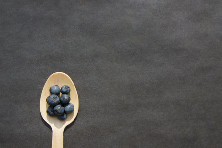 Flat lay of recycled spoon and juicy fresh blueberries on rough table. Space for text. Isolated ripe sweet bilberry fruits in eco spoon on black background. Copyspace. Healthy raw vegetarian foodの写真素材
