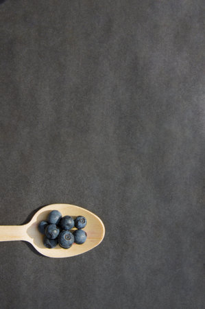 Flat lay of recycled spoon and juicy fresh blueberries on rough table. Space for text. Isolated ripe sweet bilberry fruits in eco spoon on black background. Copyspace. Healthy raw vegetarian foodの写真素材