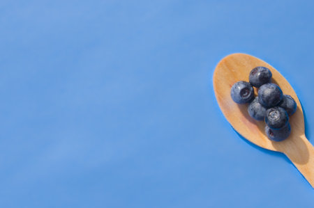 Flat lay of recycled spoon and juicy fresh blueberries on color table. Space for text. Isolated ripe...