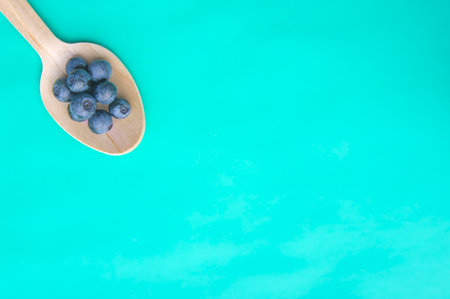 Flat lay of recycled spoon and juicy fresh blueberries on color table. Space for text. Isolated ripe sweet bilberry fruits in eco spoon on turquoise background. Copyspace. Healthy raw vegetarian foodの写真素材