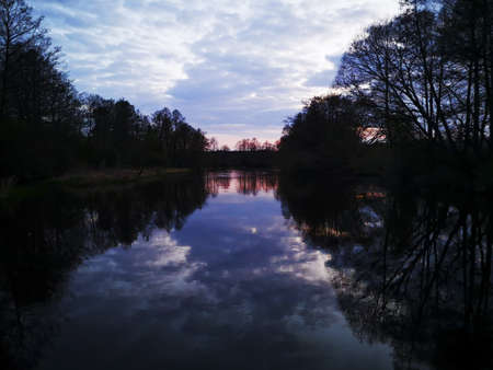Beautiful reflection of autumn trees, clouds and fading orange sunset in the river in the belarusian...