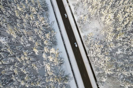 Aerial view of asphalt highway leading through frosty winter forests and groves covered with hoarfrost and snow. Drone photo of black road line and trees with chill snow in mountains. Christmas themeの写真素材