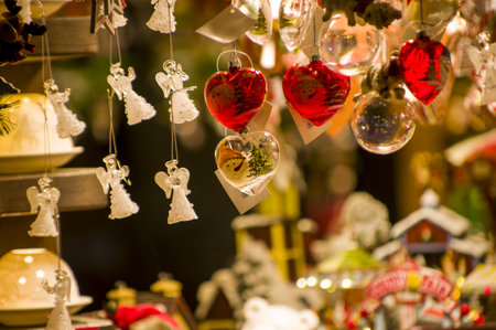 Advent Bazaar Stalls with glass, wooden, ceramic christmas souvenirs in a shop. Close up of festive decorations for tree in winter street night market during new year's holiday. Illuminated fair kioskの写真素材