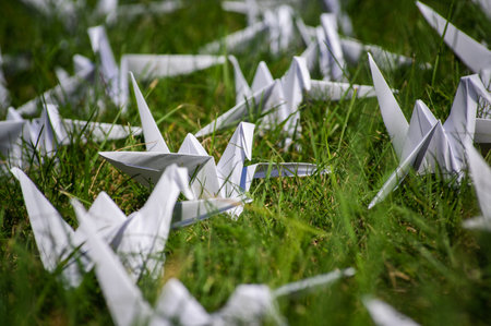 Japanese folded Origami cranes on fresh grass. Hundreds handmade paper birds on green field with copy space. 1000 thousand crane tsuru sculpture topic. Symbol of peace, faith, health, wishes and hopeの写真素材