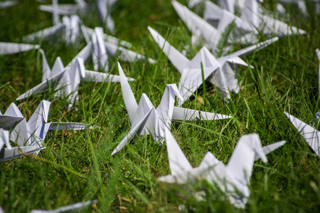 Japanese folded Origami cranes on fresh grass. Hundreds handmade paper birds on green field with...