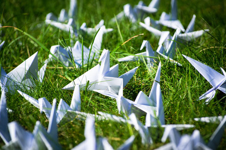 Japanese folded Origami cranes on fresh grass. Hundreds handmade paper birds on green field with copy space. 1000 thousand crane tsuru sculpture topic. Symbol of peace, faith, health, wishes and hopeの写真素材