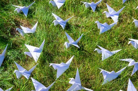 Japanese folded Origami cranes on fresh grass. Hundreds handmade paper birds on green field with copy space. 1000 thousand crane tsuru sculpture topic. Symbol of peace, faith, health, wishes and hopeの写真素材
