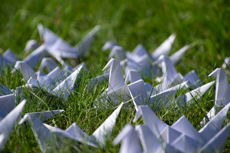 Japanese folded Origami cranes on fresh grass. Hundreds handmade paper birds on green field with copy space. 1000 thousand crane tsuru sculpture topic. Symbol of peace, faith, health, wishes and hopeの写真素材