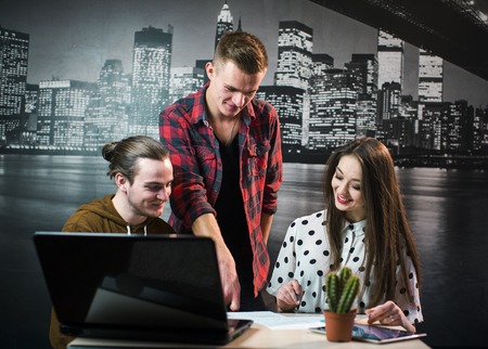 A studio shot of a teamwork support between three young designers, discussion of new ideas and explanation on the workplace before night city wallpaperの写真素材