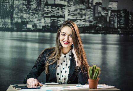 A studio shot of a beautiful woman works in economical sphere. Successfully young brunette smiling during office work on laptop before city wallpaperの写真素材