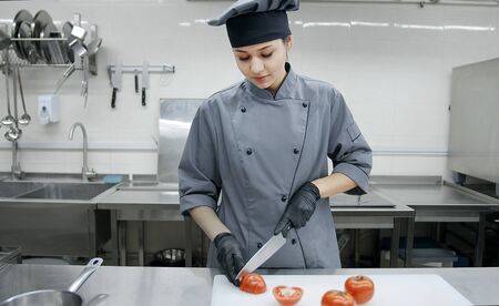 Young pretty woman chef in uniform cutting vegetables in professional kitchen, cooking and food conceptの写真素材