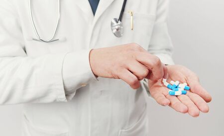 Cropped image of unrecognizable doctor having handful of blue and white gelatin capsules trying to take oneの写真素材