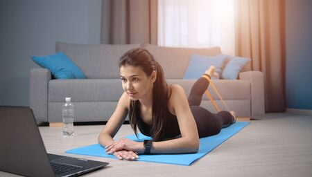 Young lady training while watching video lesson lying on stomach and lifting one leg using mini-bandの写真素材