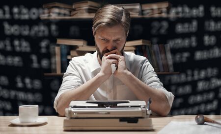 Bewildered wordsmith holding screwed paper and resting his chin on hands over bookcase on backgroundの写真素材