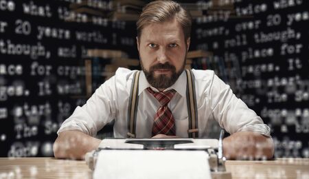 Confident writer sitting at table in front of typewriter looking at camera, front view
