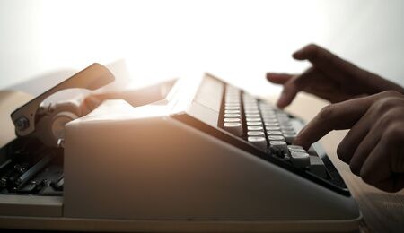 Old typewriter and male hands typing on keyboard, light flareの写真素材