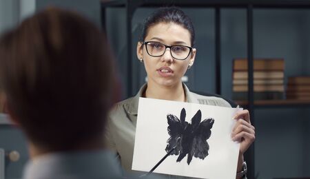 Female psychologist showing Rorschach Inkblot card to patient, view from behind client