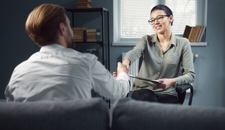 Thankful client shaking psychologists hand, male patient sitting back to cameraの写真素材