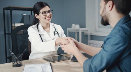 Smiling female doctor shaking hands with satisfied male patient, trust and medical ethics conceptの写真素材