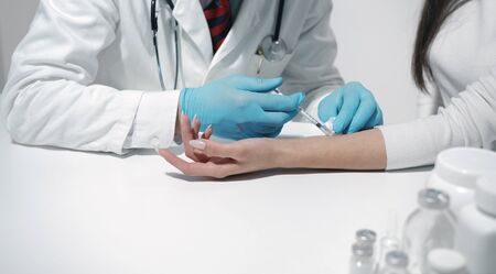 Close-up of doctors hands in blue latex gloves making injection to female patients forearmの写真素材