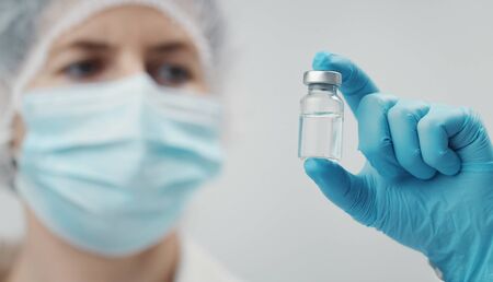 Closeup of medical doctor holding vaccine in transparent glass vial between fingers, focus on bottleの写真素材
