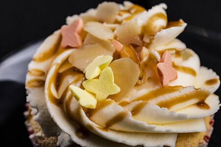 Closeup of cupcake buttercream topping drizzled with caramel and colorful butterfly shaped sprinklesの写真素材