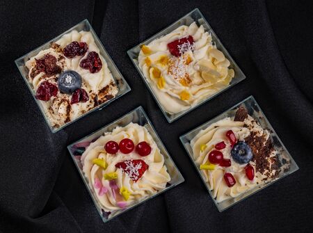 Group of square glass bowls with dessert or icecream with different topping on dark fabric, top viewの写真素材