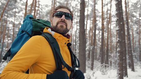 Portrait of bearded backpacker in sunglasses with trekking gear hiking in winter woods, half-bodyの写真素材