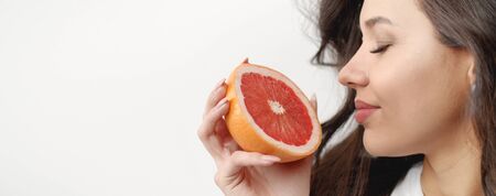 Profile of glad young woman face with closed eyes next to half of juicy grapefruit in her handの写真素材