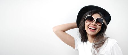 Portrait of young grinning brunette wearing sunglasses and black hat, isolated on white backgroundの写真素材