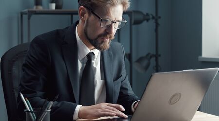 Cropped portrait of businessman in formal suit and eyewear working with laptop sitting in office