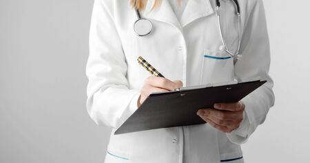 Midsection of female doctor holding clipboard and pen filling out medical document, isolated on whiteの写真素材