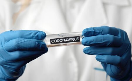 Close-up of doctor's hands in latex gloves holding vaccine test tube with coronavirus inscription