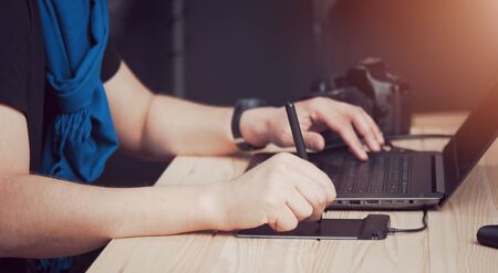 Close-up of male photographer hands using laptop keyboard and drawing tablet, side view