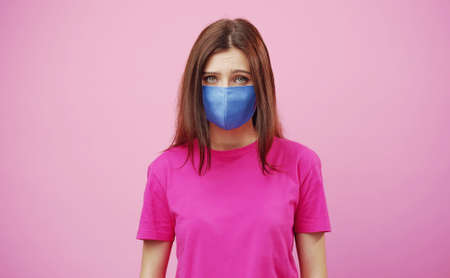 Portrait of young tearful woman wearing face mask looking at camera, isolated pink backgroundの写真素材