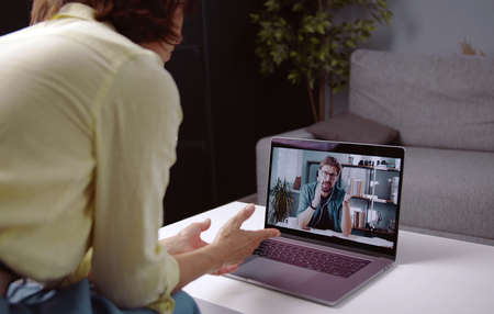 Rear view of woman staying at home talking to man using video call on laptop, cropped shot