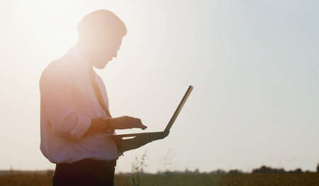 Side view of businessman holding laptop and typing keyboard standing in countryside, low angleの写真素材
