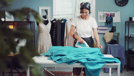 Positive woman ironing fabric preparing for sewing while working in fashion clothing studio