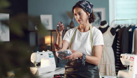 Woman seamstress choosing accessories for dressmaking standing in sewing workshopの写真素材