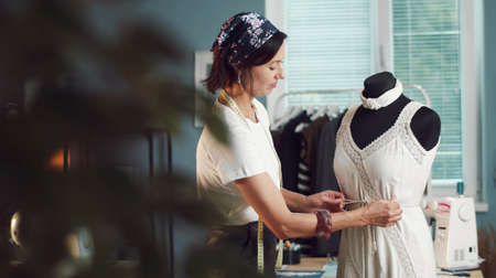 Female dressmaker adjusting dress on mannequin in sewing studio, handmade clothes concept