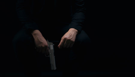 Close up of male hands holding weapon over black background. Gangster in suit holding gun in hands....