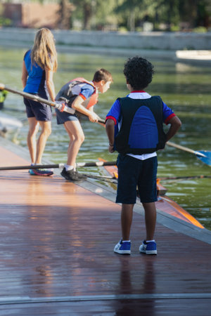 10 year old boy in blue lifejacket standing on his back on dock watching his buddies out of focus...