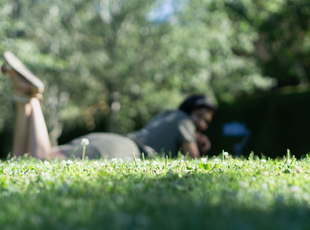 A woman is lying on the grass in a park. The grass is green and the sky is blueの写真素材